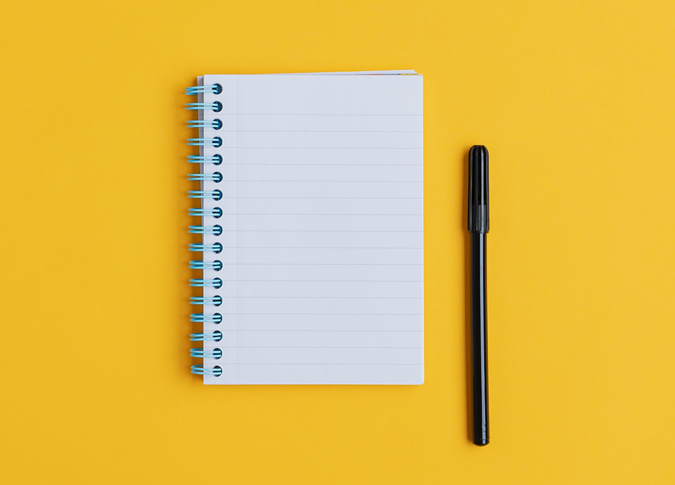 a blank notepad with a pen sitting next to it on a yellow background
