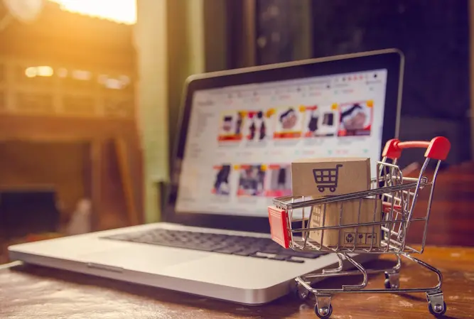 miniature shopping cart in front of laptop set to ecommerce site